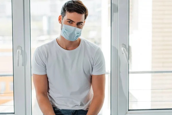 Man in medical mask looking at camera near window at home — Stock Photo