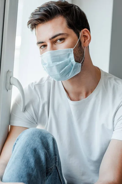 Людина в медичній масці дивиться на камеру біля вікна — стокове фото