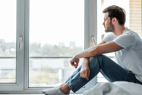 Selektiver Fokus eines gutaussehenden Mannes, der zu Hause auf der Fensterbank sitzt — Stockfoto