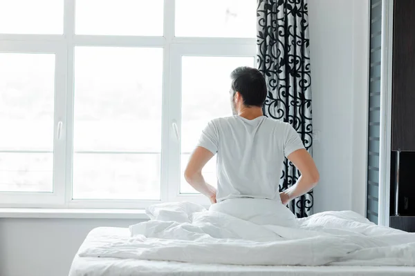 Back view of man looking at window while sitting on bed at home — Stock Photo