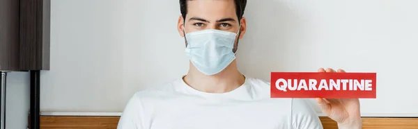 Uomo in maschera medica in possesso di carta con iscrizione di quarantena a casa, coltura panoramica — Foto stock