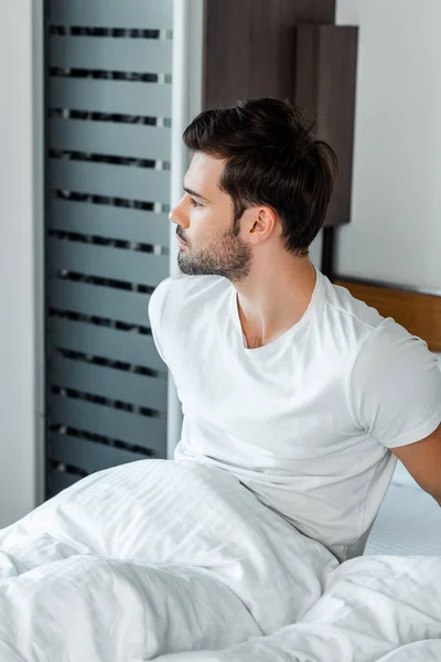 Hombre guapo mirando mientras está sentado en la cama - foto de stock