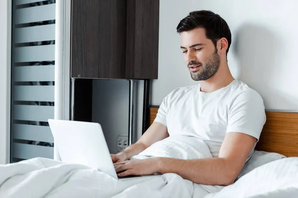 Selective focus of handsome bearded man using laptop on bed — Stock Photo