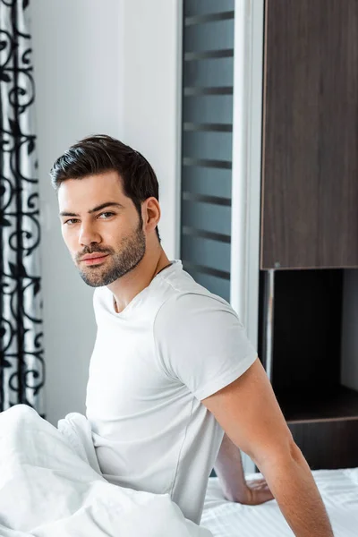 Side view of handsome man looking at camera while sitting on bed — Stock Photo