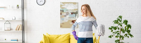 Website header of woman with hand on hip and mop looking away and smiling in living room — Stock Photo