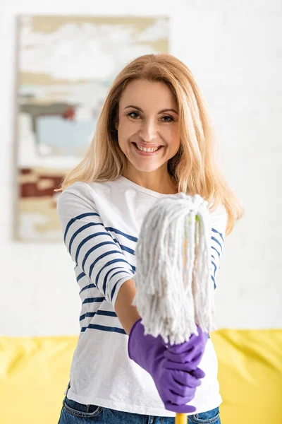 Front view of beautiful woman smiling, looking at camera and showing mop in living room — Stock Photo