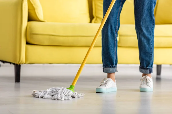 Vista recortada del piso de fregona de mujer con fregona en la sala de estar - foto de stock