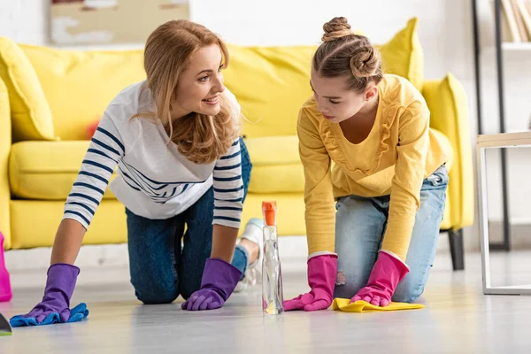 Madre e hija a cuatro patas limpiando el suelo con trapos en la sala de estar - foto de stock