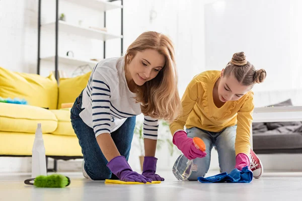 Mãe e filha com garrafa de spray e trapos limpando o chão perto da escova na sala de estar — Fotografia de Stock