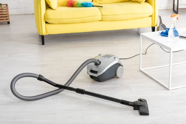 Vacuum cleaner near coffee table and sofa with feather duster in living room — Stock Photo