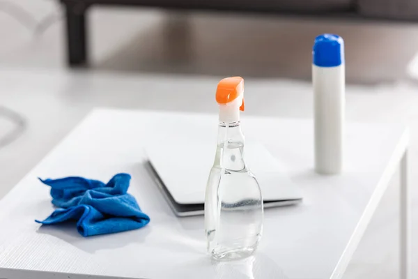 Mesa de centro con portátil, botellas de spray y trapo en la sala de estar - foto de stock