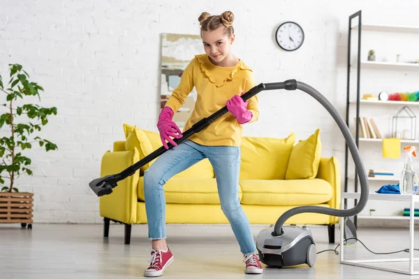 Enfant imitant jouer de la guitare avec aspirateur, souriant et regardant la caméra dans le salon — Photo de stock