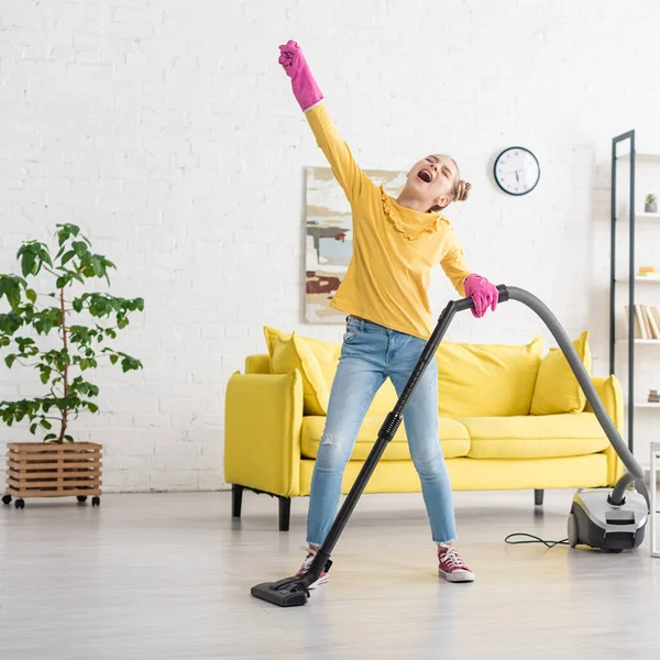 Nettes Kind mit geschlossenen Augen und ausgestreckter Hand singt mit Staubsauger im Wohnzimmer — Stockfoto