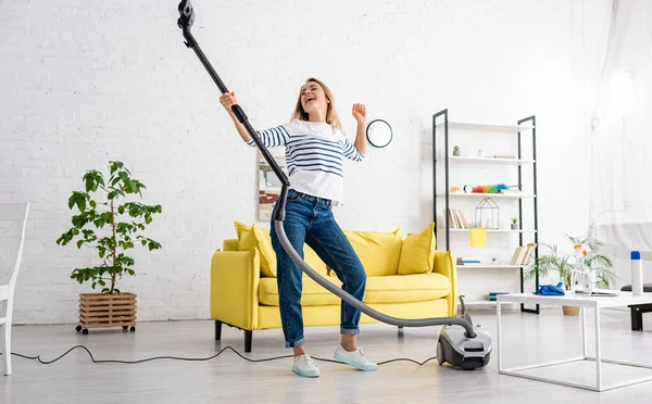 Woman singing with vacuum cleaner near sofa and coffee table in living room — Stock Photo