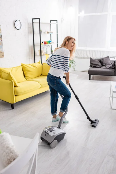 Attraktive Frau lächelt und räumt mit Staubsauger im Wohnzimmer auf — Stockfoto