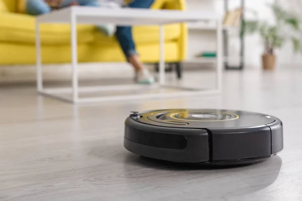 Cropped view of mother with daughter on sofa and robotic vacuum cleaner on floor in living room — Stock Photo