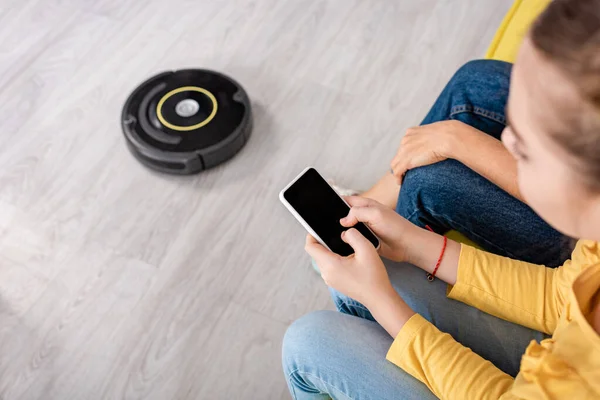Cropped view of child with smartphone and mother near robotic vacuum cleaner on floor in living room — Stock Photo