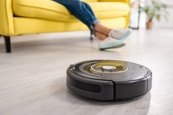 Cropped view of female legs with robotic vacuum cleaner on floor in living room — Stock Photo