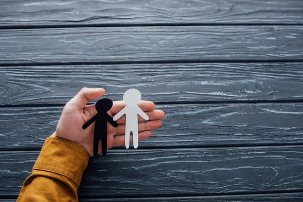 High angle view of man holding white and black human figures on dark wooden surface — Stock Photo