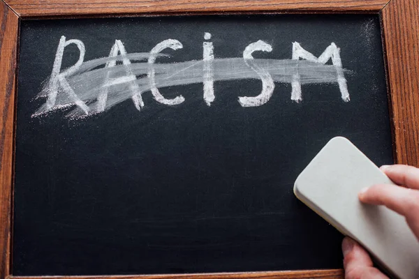 Cropped view of man holding chalkboard cleaner near lettering racism — Stock Photo