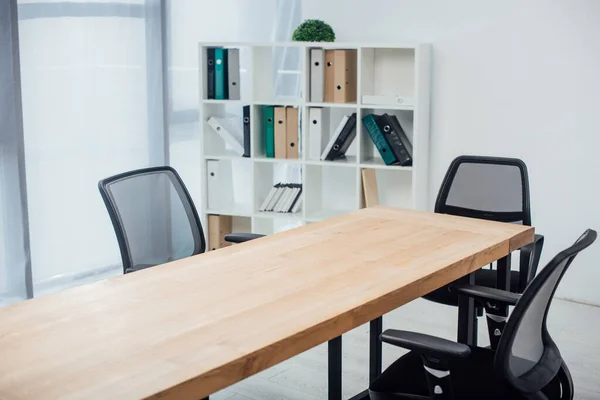 Mesa de madeira e cadeiras perto do rack com pastas de papel no escritório — Fotografia de Stock