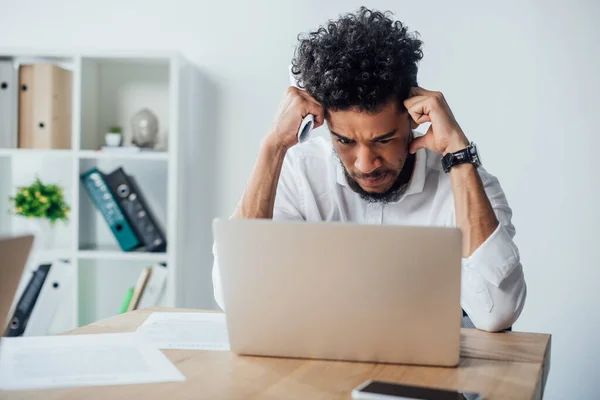 Selective focus of pensive african american businessman looking at laptop and holding document in office — Stock Photo