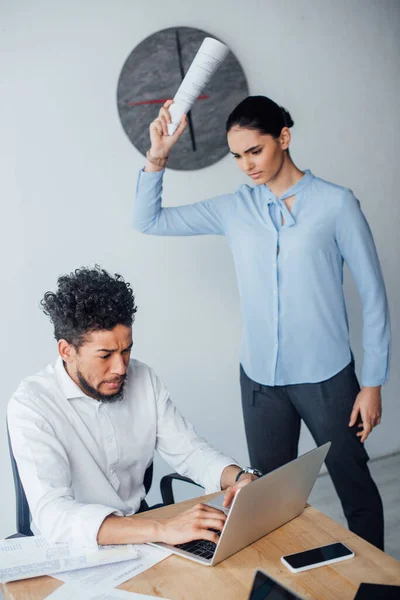 Selective focus of scared african american businessman using laptop near angry mexican businesswoman — Stock Photo