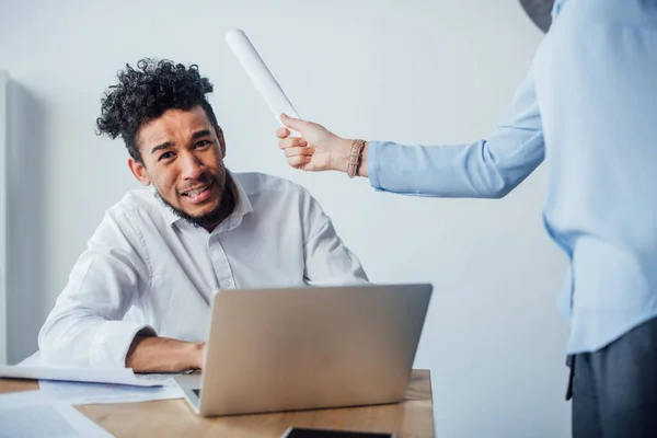 Selektiver Fokus eines verängstigten afrikanisch-amerikanischen Mannes, der in die Kamera blickt, in der Nähe einer Geschäftsfrau, die Papier im Büro hält — Stockfoto