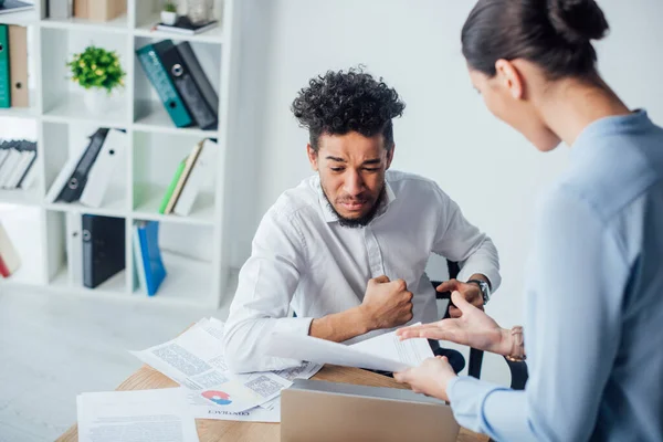 Selective focus of businesswoman pointing at papers near offended african american man at table in office — Stock Photo