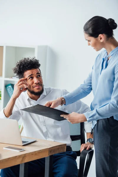 Selective focus of african american man looking at mexican businesswoman with clipboard in office — Stock Photo