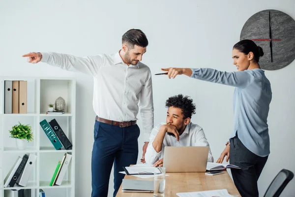 Multiethnic business people pointing with fingers at african american businessman at table in office — Stock Photo