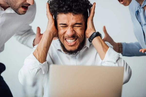 Селективный фокус африканского американского бизнесмена, закрывающего уши перед ссорящимися коллегами в офисе — стоковое фото
