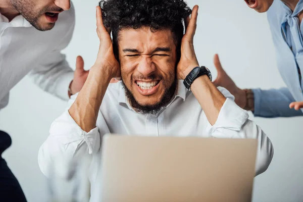 Selective focus of african american businessman covering ears near quarreling colleagues in office — Stock Photo