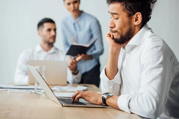 Selective focus of african american businessman using laptop near multiethnic colleagues in office — Stock Photo