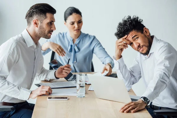 Selective focus of pensive african american businessman looking at camera near multiethnic colleges in office — Stock Photo