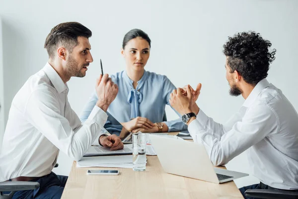 Enfoque selectivo de la gente de negocios multiétnicos mirando a un colega afroamericano cerca de computadoras portátiles y papeles en la oficina - foto de stock