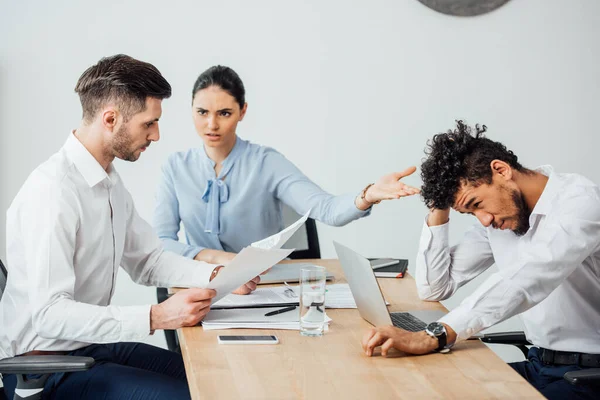 Donna d'affari messicana arrabbiata che indica collega afroamericano a collega con documenti in carica — Foto stock