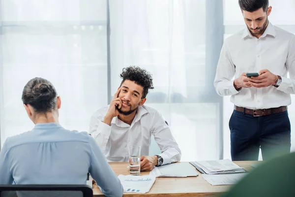 Selective focus of african american man looking at camera near business people in office — Stock Photo