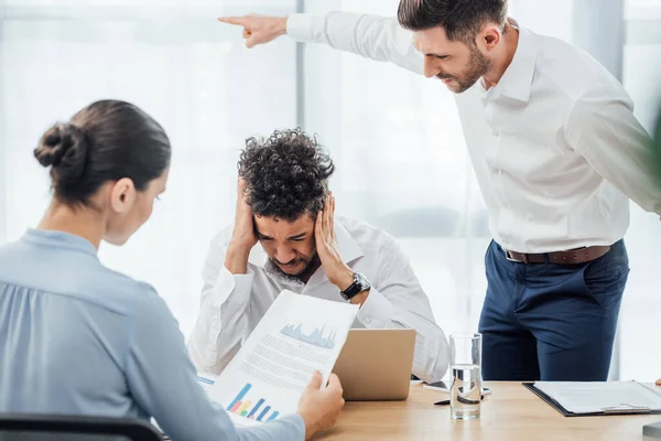 Selective focus of businessman pointing with finger near upset african american colleague in office — Stock Photo