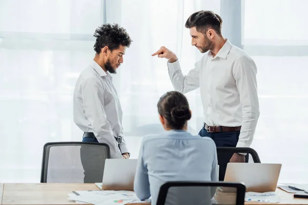 Selektiver Fokus eines Geschäftsmannes, der mit dem Finger auf beleidigte afrikanische Amtskollegin zeigt — Stockfoto