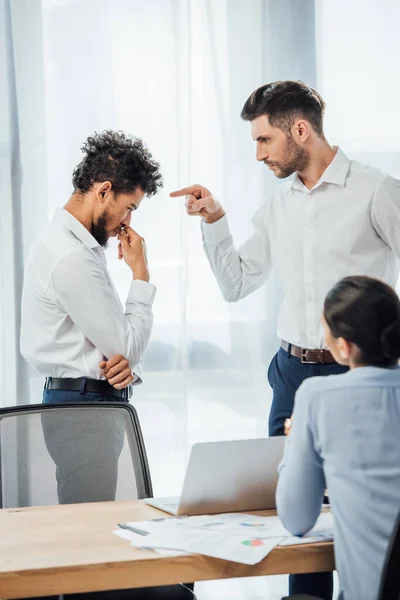 Selective focus of businessman pointing at offended african american colleague in office — Stock Photo