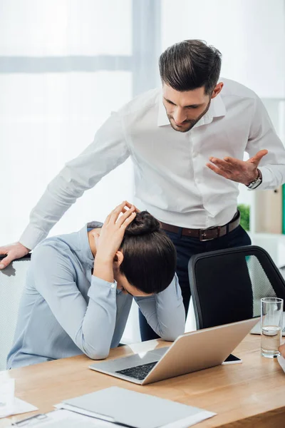 Foco seletivo de homem de negócios apontando com a mão perto de colega mexicano triste à mesa no escritório — Fotografia de Stock