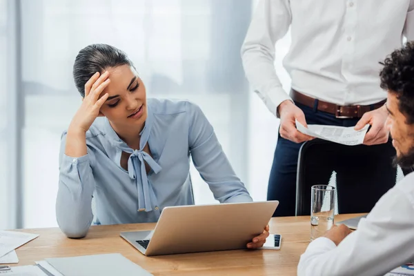 Focus selettivo della donna d'affari messicana sorridente che utilizza il computer portatile vicino al collega afroamericano in carica — Foto stock