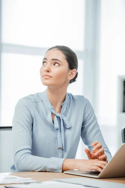 Enfoque selectivo de la hermosa mujer de negocios mexicana mirando hacia otro lado mientras usa el portátil en la oficina - foto de stock