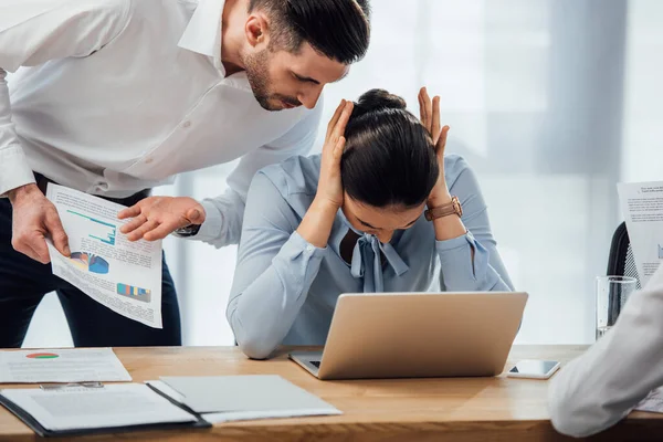 Focus selettivo dell'uomo d'affari che indica i documenti vicino alle orecchie cowering collega messicano in carica — Foto stock