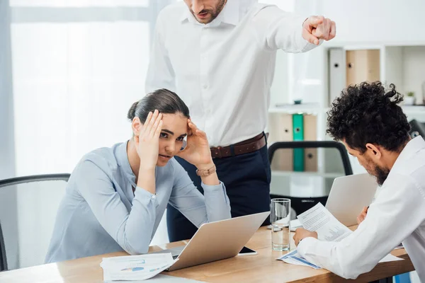 Uomo d'affari che punta con il dito vicino sconvolto donna d'affari messicana a tavola in ufficio — Foto stock