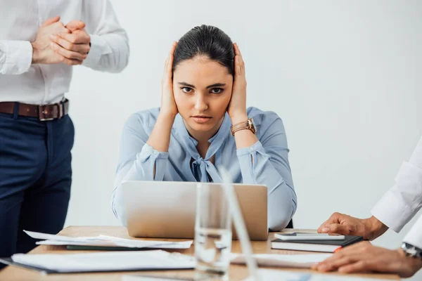 Selective focus of mexican businesswoman covering ears near multiethnic colleagues in office — Stock Photo