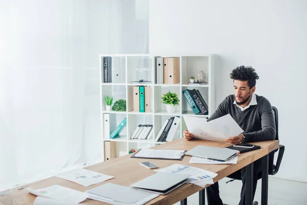 Селективный фокус африканского американского бизнесмена, работающего с бумагами за столом в офисе — стоковое фото