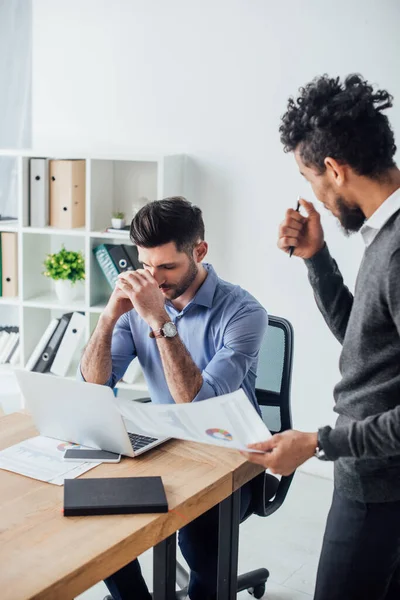 Selective focus of african american businessman holding document near colleague in office — Stock Photo