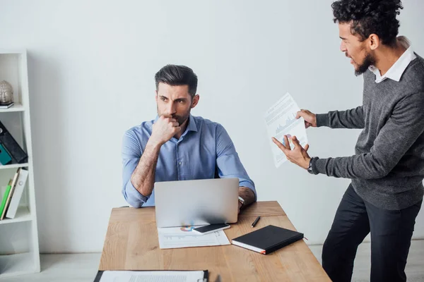 Angry african american businessman quarreling at colleague near laptop in office — Stock Photo